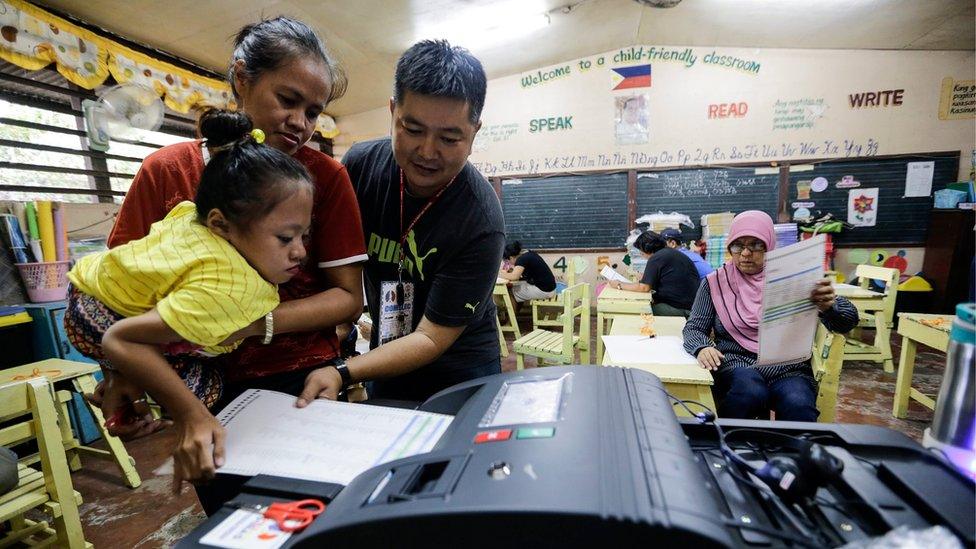 Fife Vanice Dayola, 21, who was born with bone misalignment, is carried by her mother Rowena Dayola and assisted by an election worker, as she casts her vote by inserting her ballot into a machine in a school polling station in Davao city, 9 May 2016