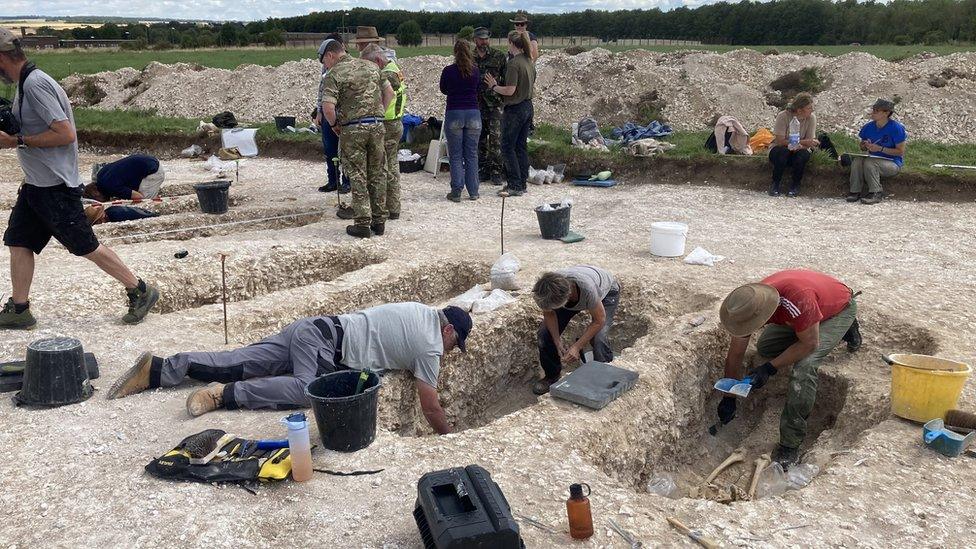 People leaning into grave sites on a dig site