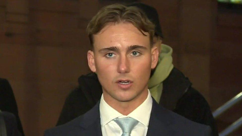 A young man in a suit speaks outside a court