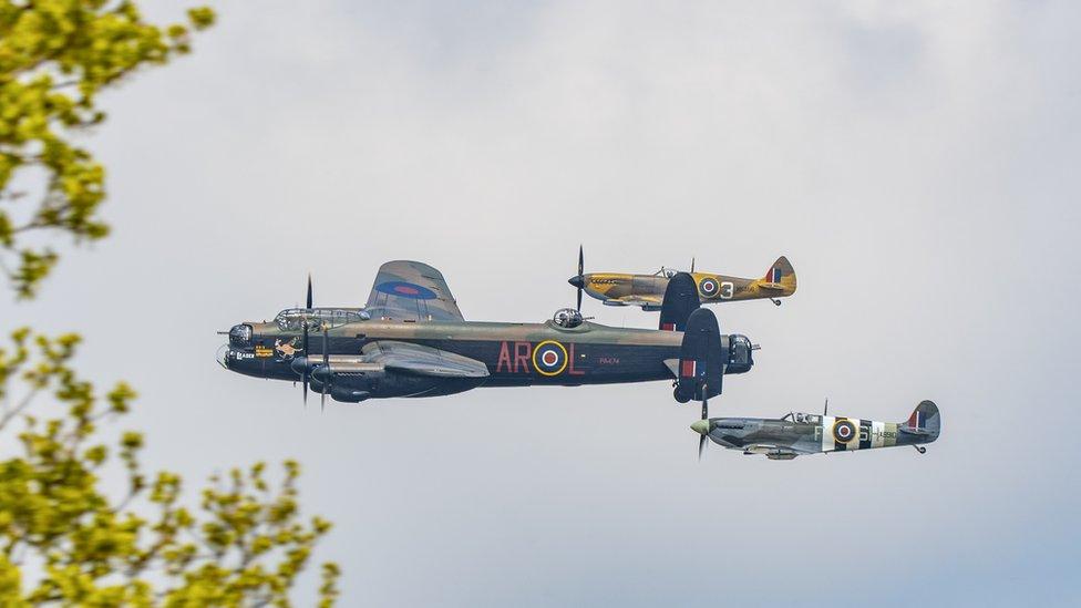 A Lancaster Bomber flies through the sky flanked by two Spitfires