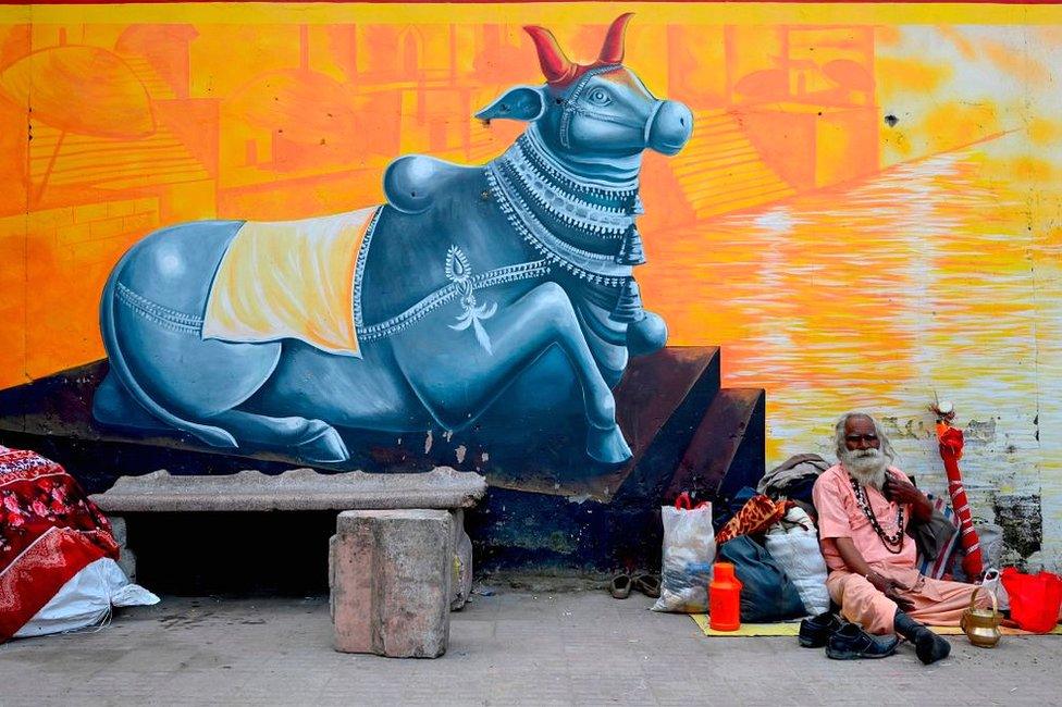 A Sadhu (Hindu holy man) sits besides a graffiti on the banks of the River Ganges during Makar Sankranti, a day considered to be of great religious significance in the Hindu mythology, on the first day of the religious Kumbh Mela festival in Haridwar on 14 January 2021