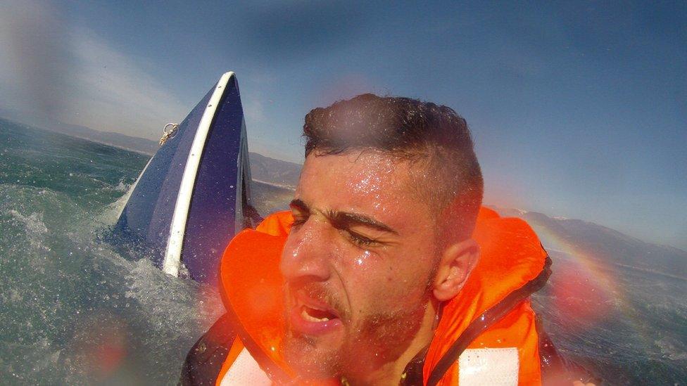 A migrant, identified as 20-year old Pelen Hussein from Syria, with a capsized boat in the background, is rescued by a member of the Turkish Coast Guard Air Command in the Aegean Sea off the waters of Edremit bay, Turkey February 8, 2016, in this handout photo provided by the Turkish Coast Guard Command