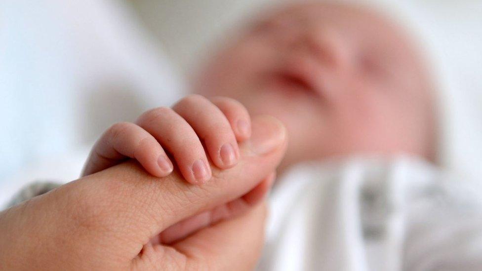 A newborn baby grasping the thumb of her mother,