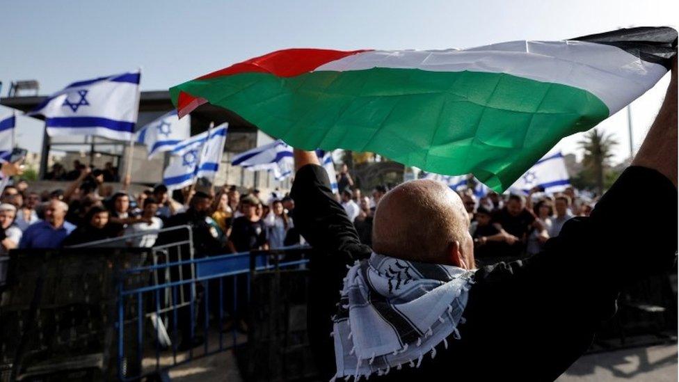 Palestinian man holds Palestinian flag opposite Israeli flags in Jerusalem (29/05/22)