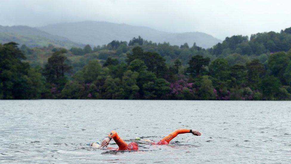 Two swimmers wearing orange suits take part in the Great North Swim Run endurance race at Lake Windermere in June 2019