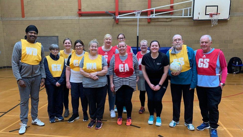 Netball players gathered for photo, wearing red and yellow bibs.