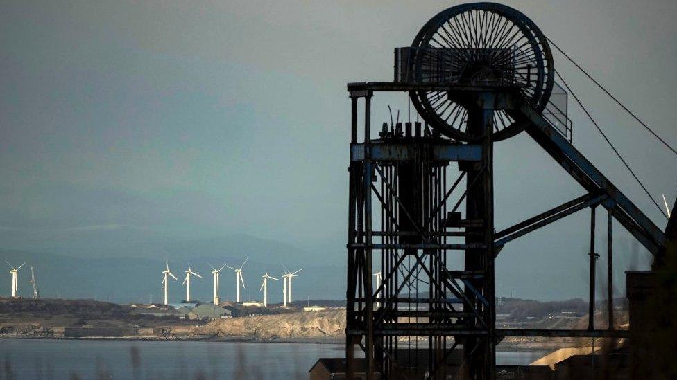 Old fashioned coal mine wheel silhouetted against the sea