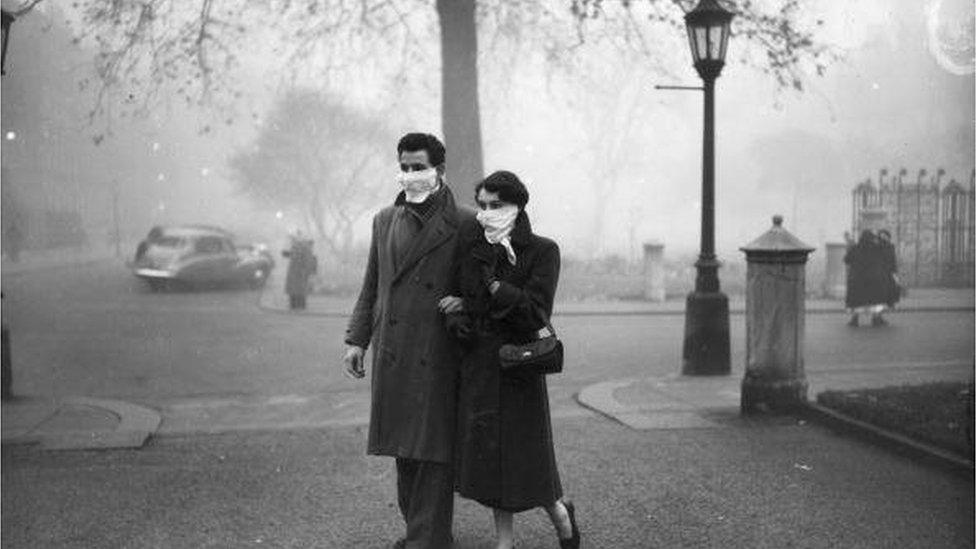 A couple walking in London wearing smog masks on a foggy day