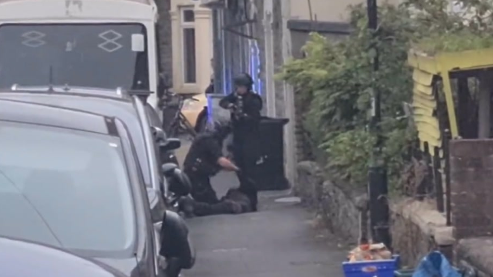 Man laying on the ground being arrested by armed policeman