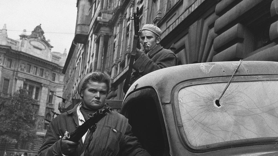 Two Hungarian freedom fighters stand armed by a truck in Budapest during the Hungarian Revolution of 1956.