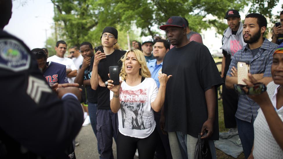 Neighbourhood residents film a police officer with their mobile phones while speaking about police mistreatment across the street from where President Barack Obama will deliver a speech at the Salvation Army, Ray & Joan Kroc Corps Community Center May 18, 2015 in Camden, New Jersey