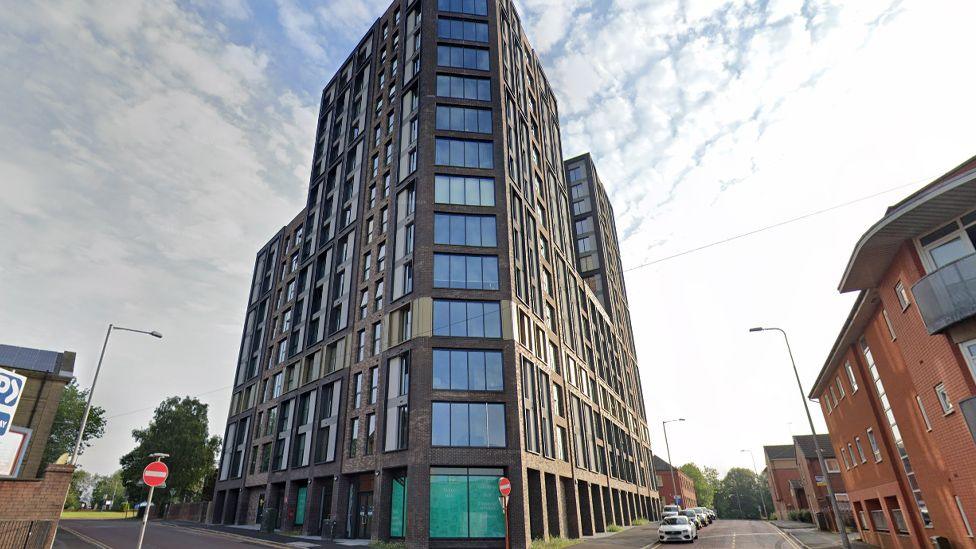 Street view image of The Exchange – a tall dark grey block of flats with many windows on a triangular plot at the junction of Pole Street and Percy Street