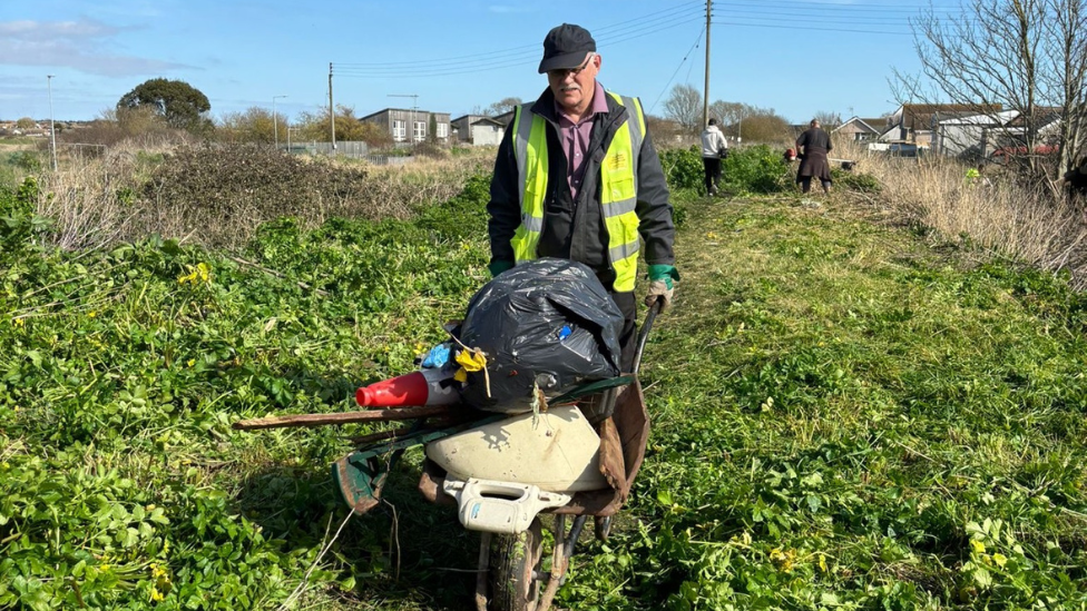 A man pushing a wheel barrow full off rubbish