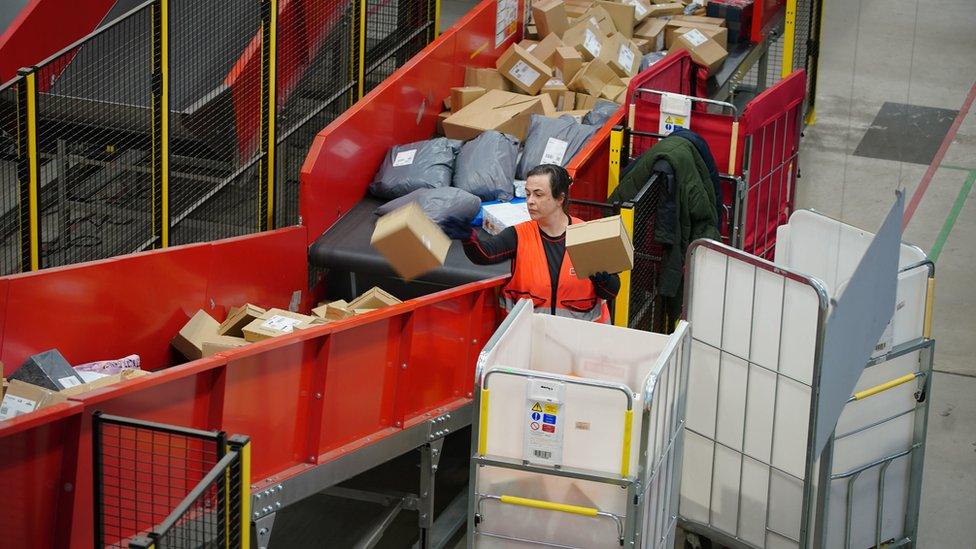 Parcels moving on the belt in a Royal Mail sorting office with a worker putting more on