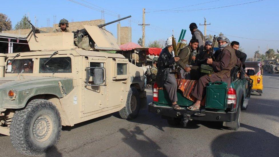 Milita fighters sit with their guns in the back of a truck passing an armed vehicle in Kunduz