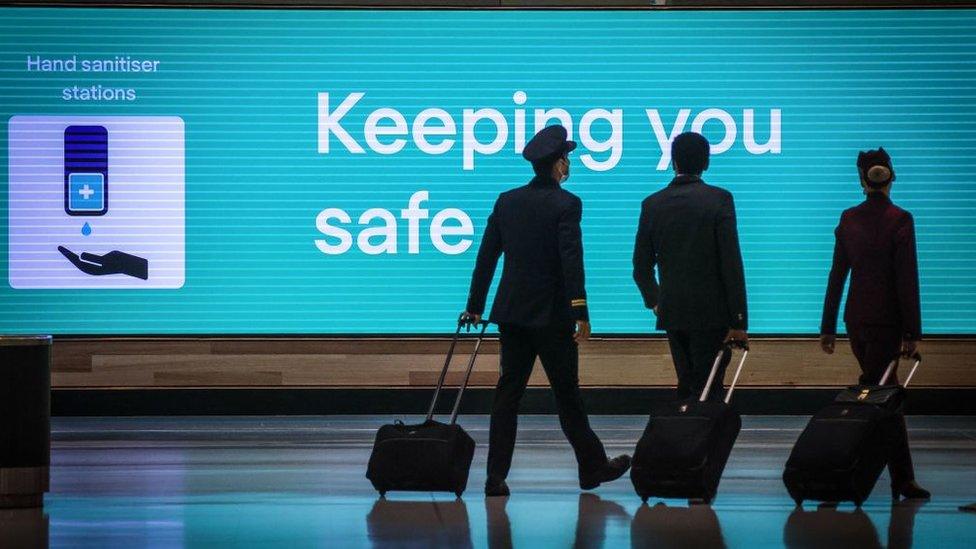 Crew walking past a sign that reads "keeping you safe" at Sydney Kingsford-Smith airport.