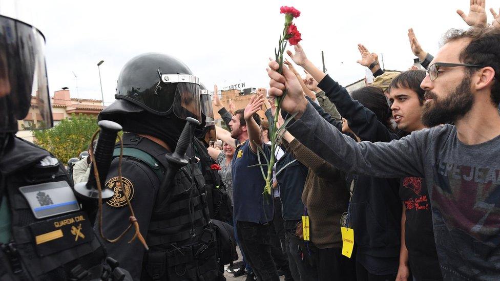 Crowds raise their arms up and a man holds red and pink flowers as police move in on members of the public gathered outside to prevent them from voting in the referendum at a polling station( October 1, 2017)