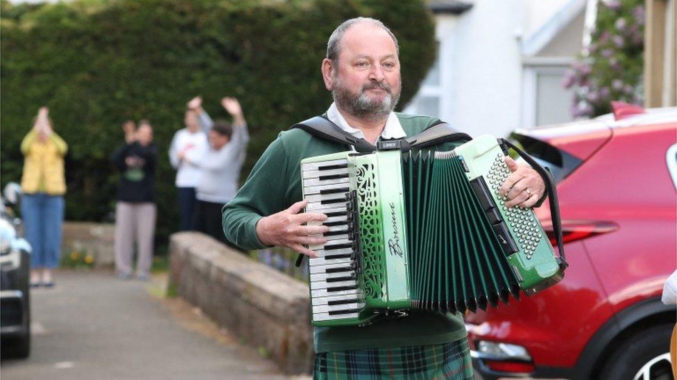 Seamus O'Sullivan playing his accordion in his street in Glasgow, as he joins in the applause to salute local heroes