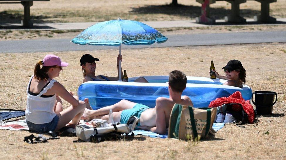 Friends sit in a kiddies paddling pool after a council parks vehicle filled their pool with water at a park in central London