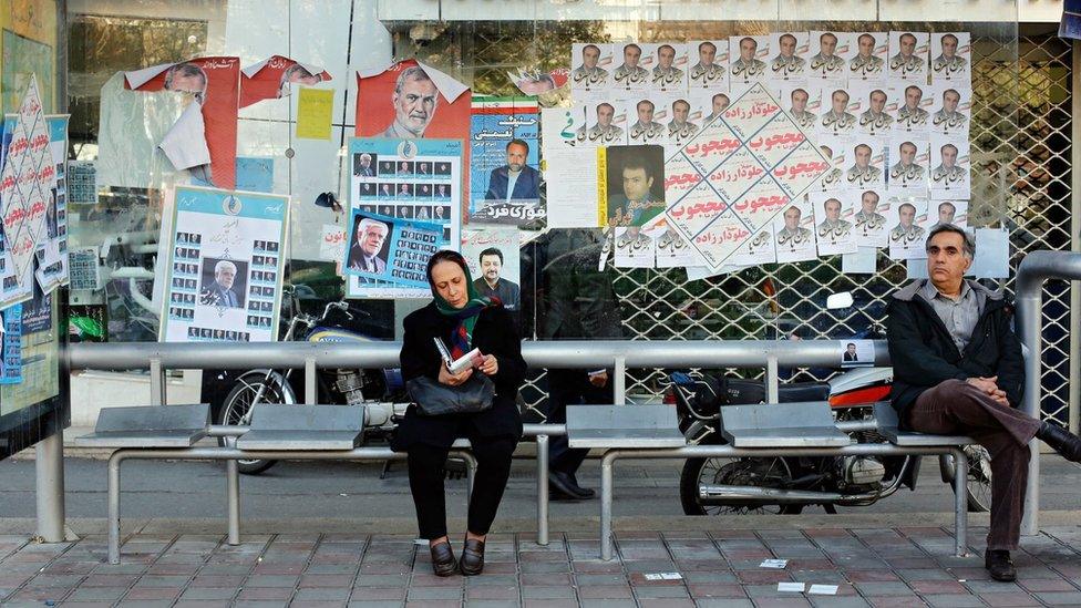 People sit at a bus stop covered in election posters in Tehran, Iran (25 February 2016)