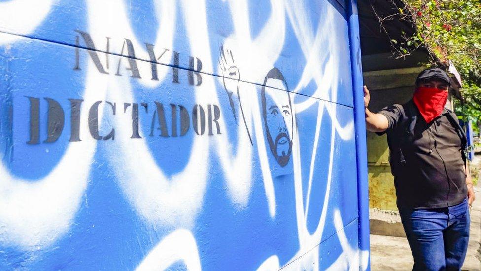 A student stands next to a graffiti against the government of Nayib Bukele in San Salvador