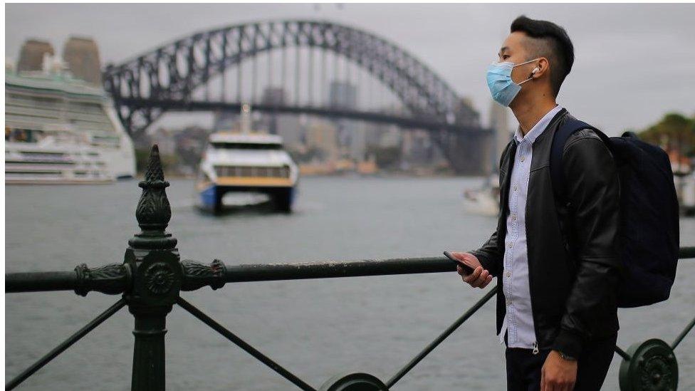 A man wears a face mask in front of the Sydney Harbour Bridge in Sydney, Australia.