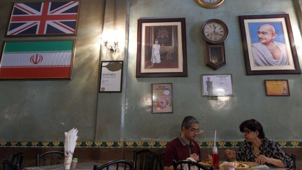 Customers eat lunch below portraits of Britain's Queen Elizabeth and Indian independence hero Mahatma Gandhi - alongside the national flags of Britain and Iran - at the Britannia Co. restaurant in Mumbai (08 April 2016)