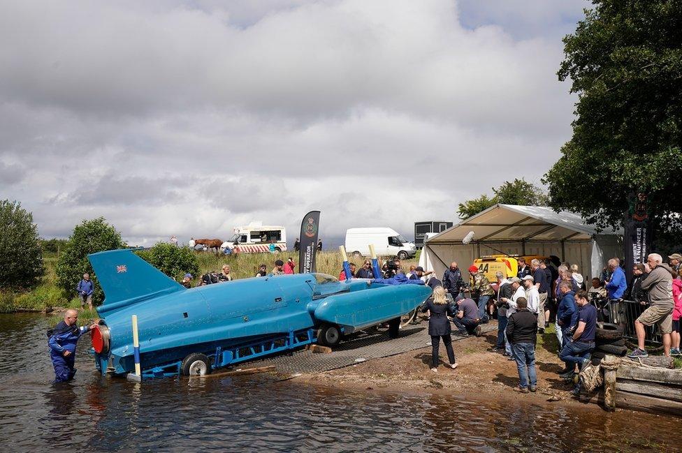 Onlookers peer from the water's edge as Bluebird is lowered on to Loch Fad