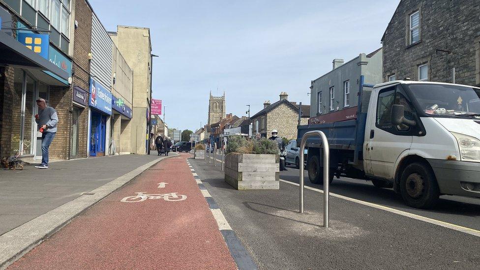 A red cycle path in Keynsham High Street with a broken white line