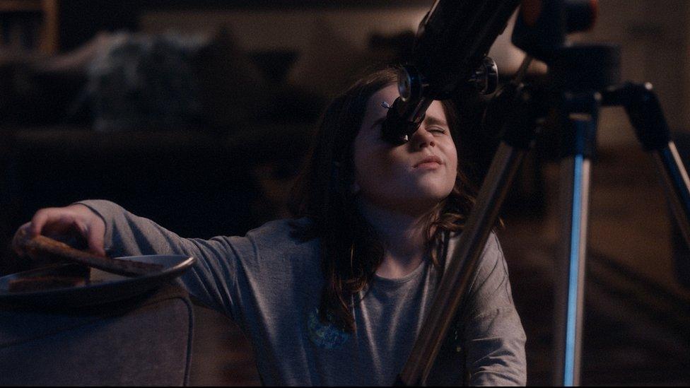 A little girl is taking at a look at the night sky using her telescope