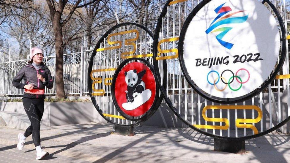 Woman runs in front of a sign for the Games in Beijing