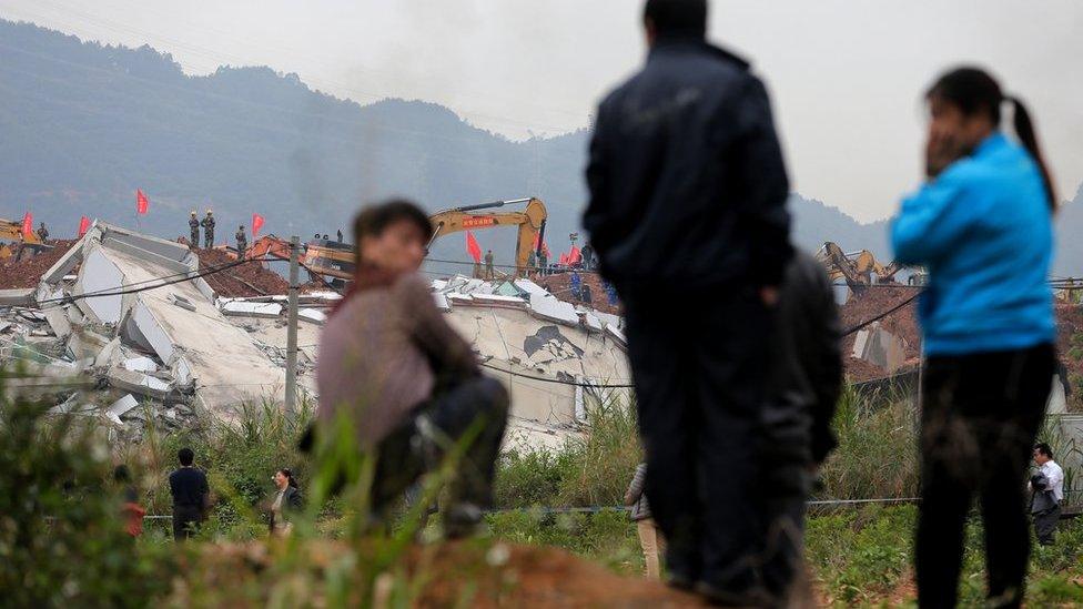 People watch rescuers using excavators dig the soil to search for potential survivors following a landslide burying buildings at an industrial park in Shenzhen, in south China's Guangdong province, Tuesday, 22 December 2015