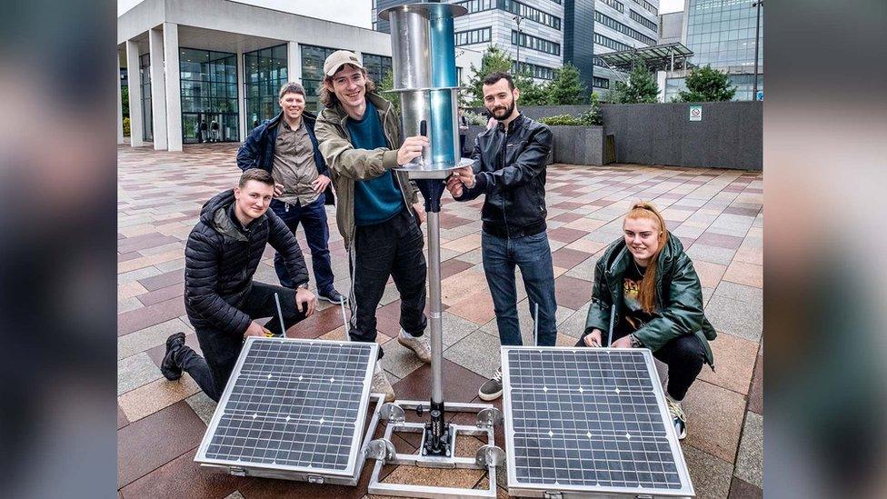 Students holding a flatpack wind turbine with solar panels