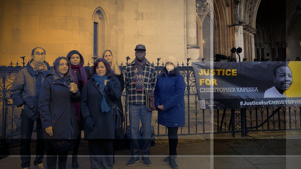 A group of campaigners gather outside a court building next to a banner reading 'Justice for Christopher Kapessa'.