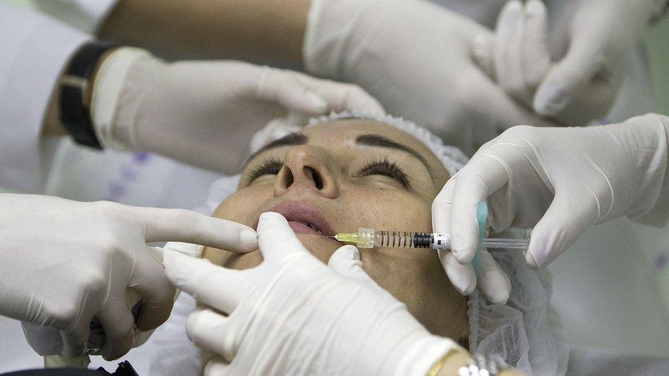 Woman's face surrounded by white gloved hands during surgery