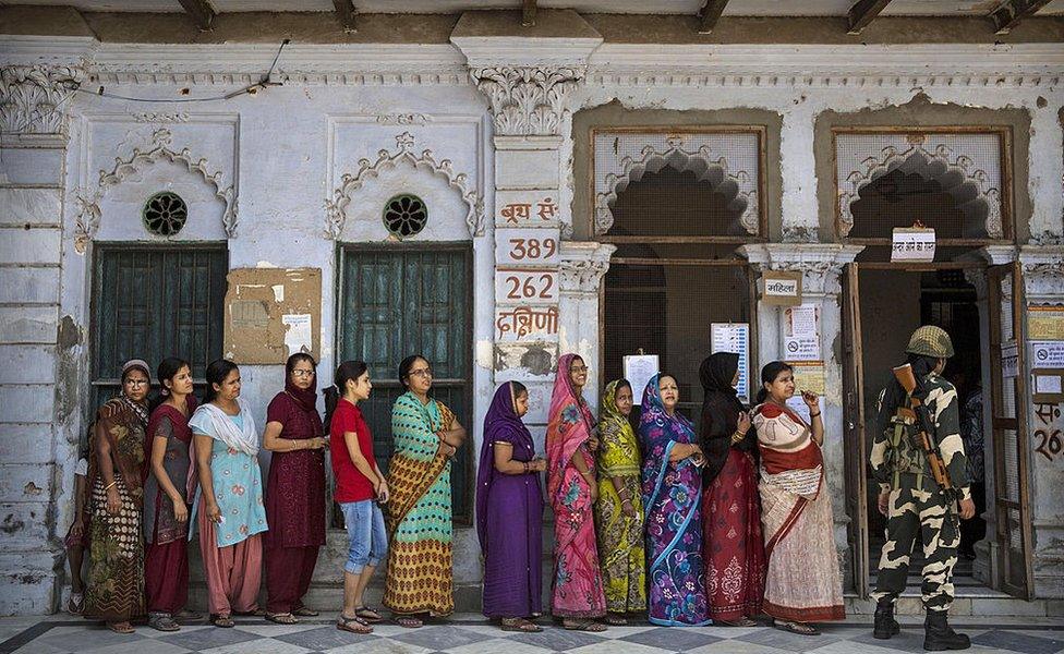 A Border Police officer stands guard as Indian women wait in line to vote at a polling station on 12 May 2014 in Varanasi, India.