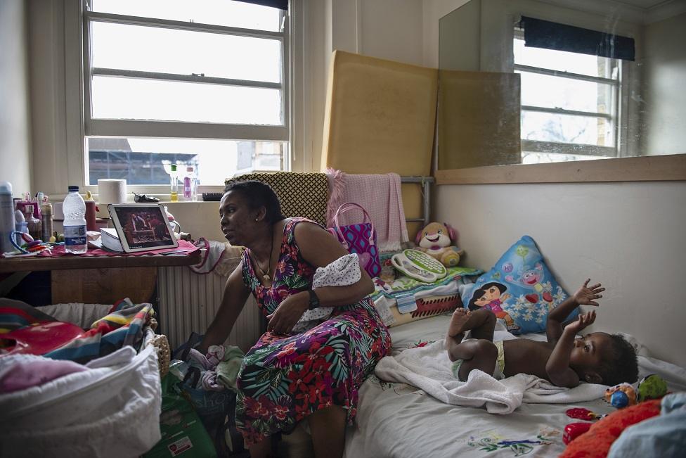 A mother and her child sit in a cluttered room