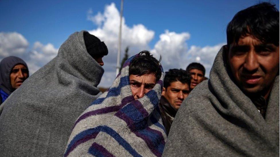 Refugees and migrants try to warm themselves up as they take a break at a petrol station before abandoning their trek to the Hungarian border, in the town of Indjija, Serbia on 5 October 2016.