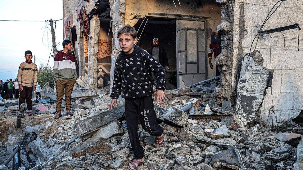 People, including children, walk through the rubble of a building heavily damaged by Israeli bombardment, in Rafah