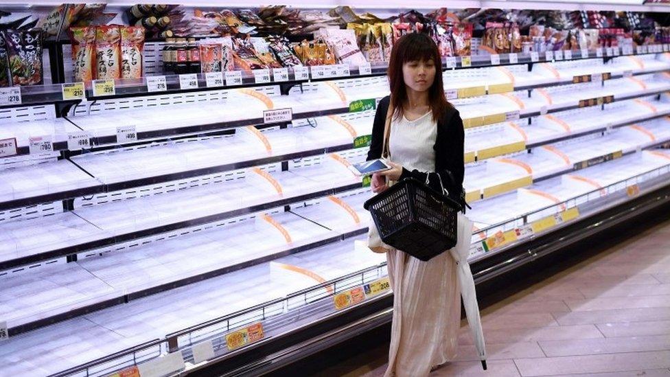 A woman walks past empty shelves in a store in Tokyo