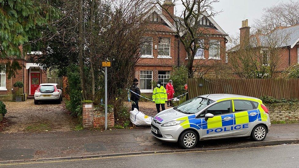 Fire-damaged house, police cordon, officers and police vehicle