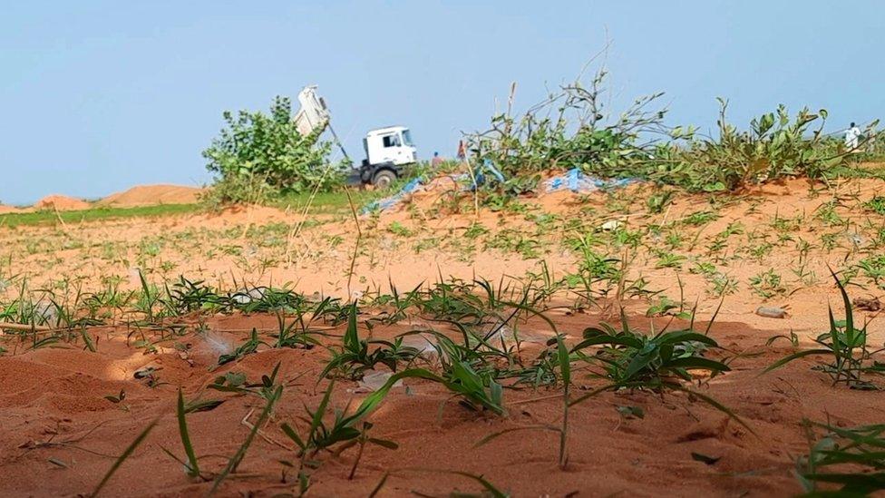 White lorry appears in the distance in middle of desert with the back of it tipped.