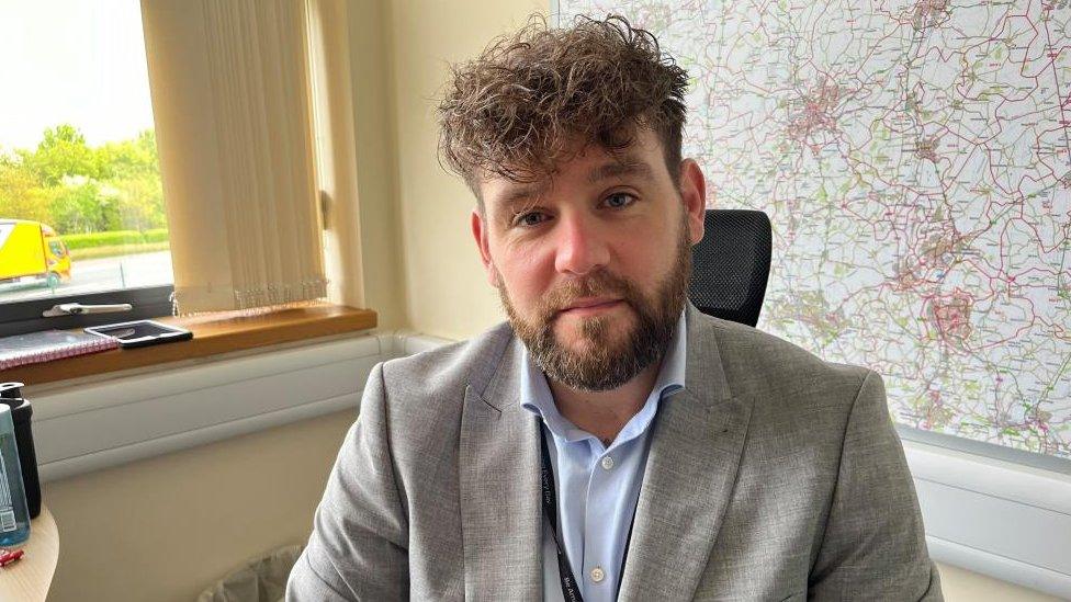 Gareth Chisholm - man with brown hair and beard sitting in front of a large map