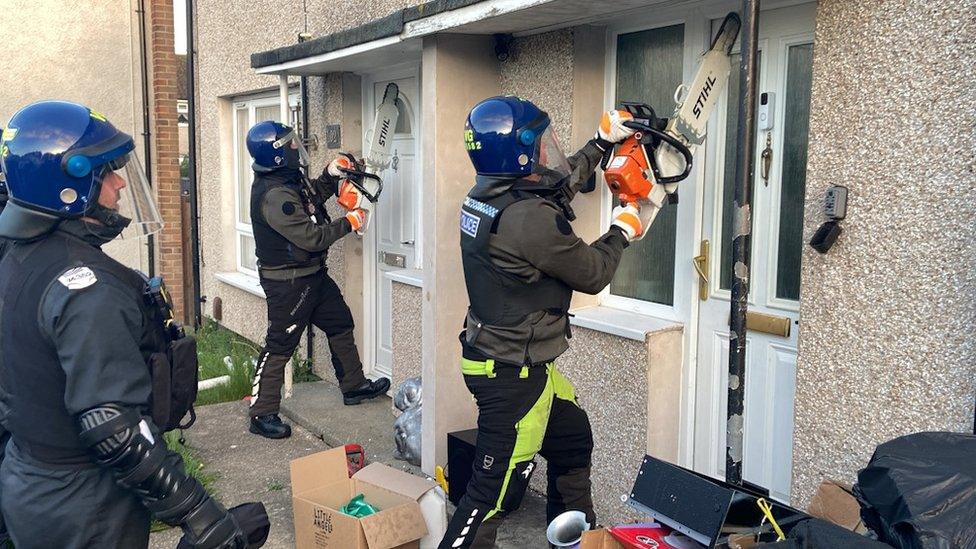 Police officers use chainsaws to enter two houses