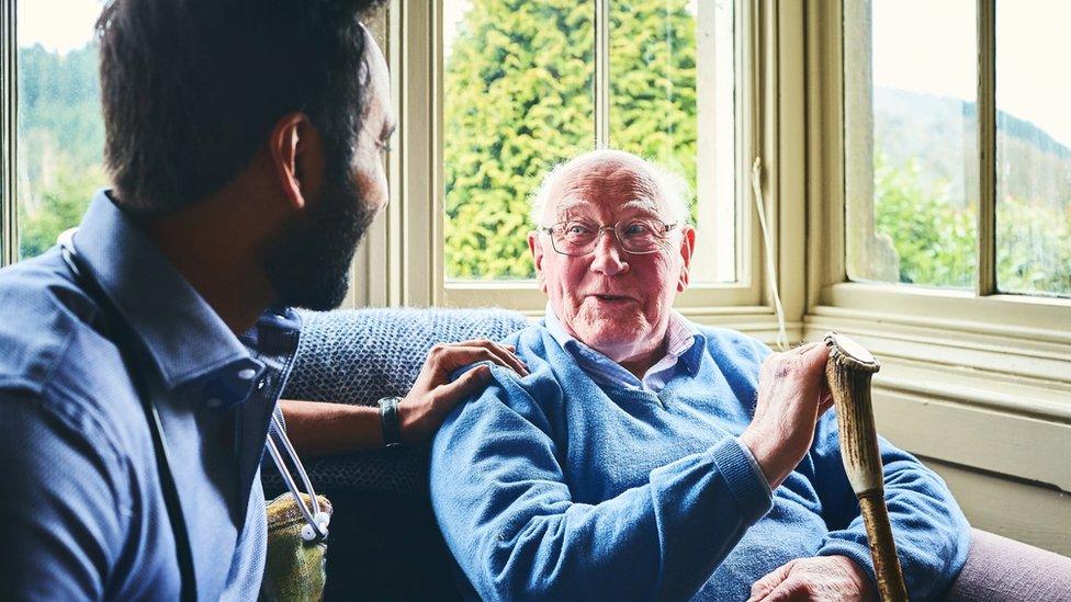 Male doctor talking with senior man in home visit