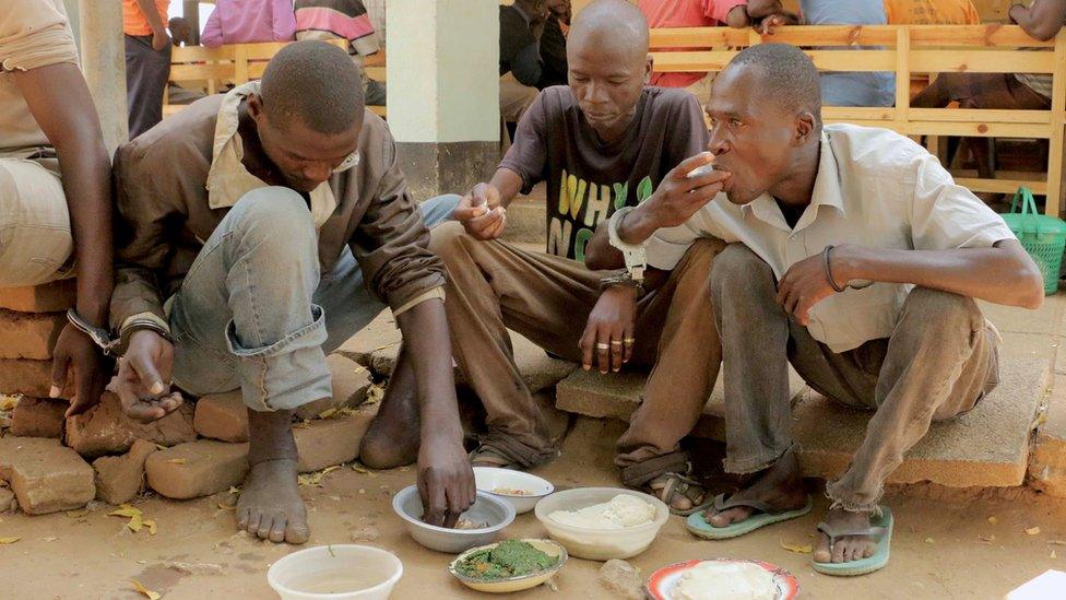 Handcuffed men eating food in the courtyard of a magistrate's court in Nsanje, Malawi - Monday 15 August 2016