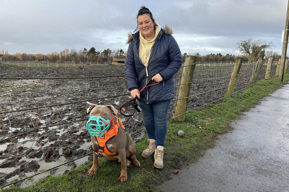 A woman holds a muzzled dog on a lead