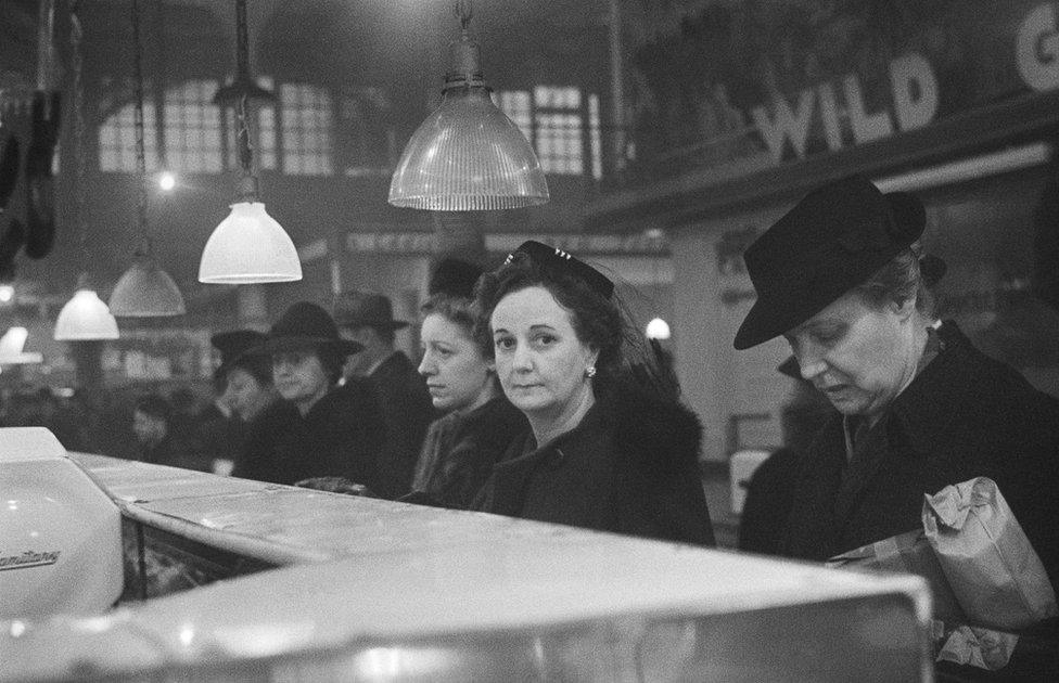 Customers waiting in line at a butcher's counter during wartime rationing. Washington Market, New York, 1941-44