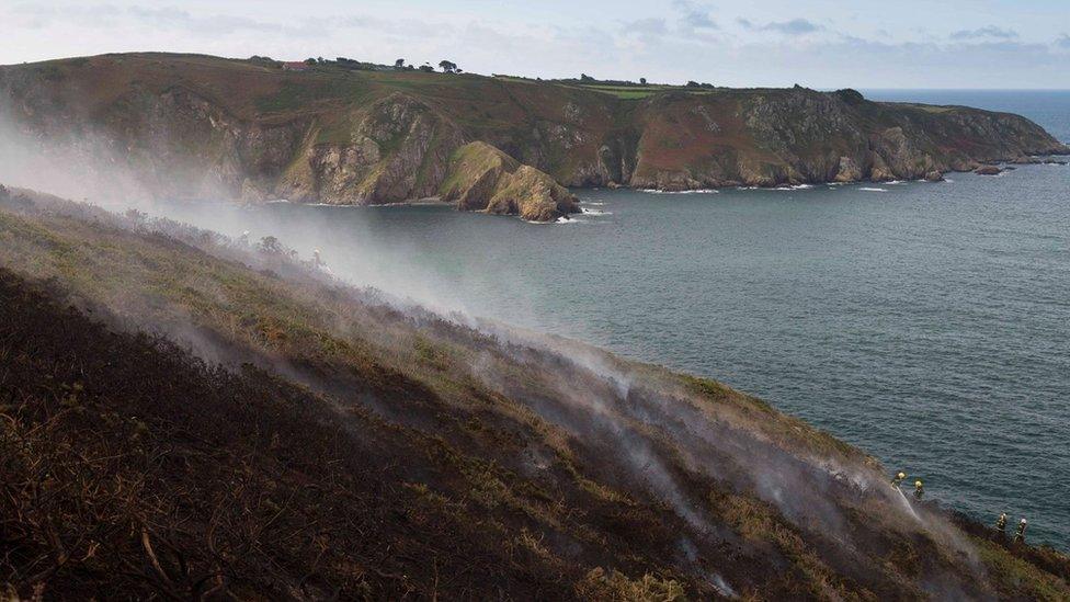 Smouldering vegetation on Sark's cliff after fire crews dampen down the area