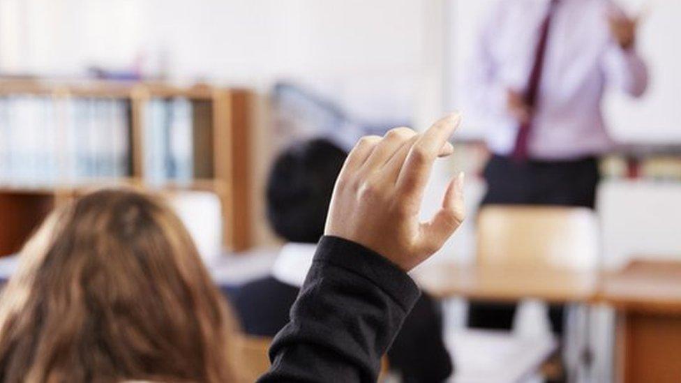 Female student raising her hand to ask a question in a classroom